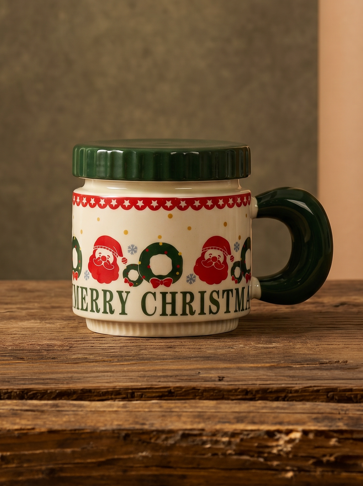 A ceramic Christmas mug with a dark green handle and lid, decorated with Santa Claus and wreath motifs and the text 'MERRY CHRISTMAS' on a cream background, set on a rustic wooden table.